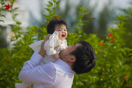 年轻，快乐，骄傲的男人，作为可爱的小女孩的父亲，抱着她的女儿在假日度假村的花园前，在家庭生活理念中一起享受户外活动