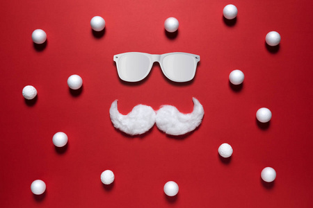 白色时髦的圣诞老人胡子，戴着红色背景的太阳镜。 新年或圣诞节最低概念。