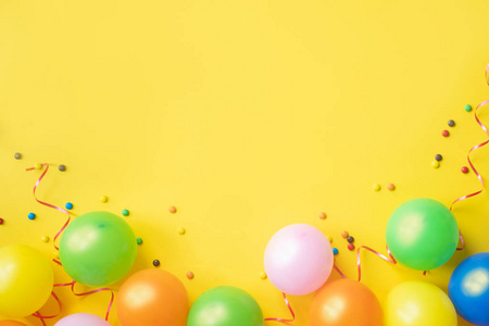 一堆五颜六色的气球，纸屑和糖果在黄色的桌子顶部的视图。 生日派对背景。 节日贺卡。