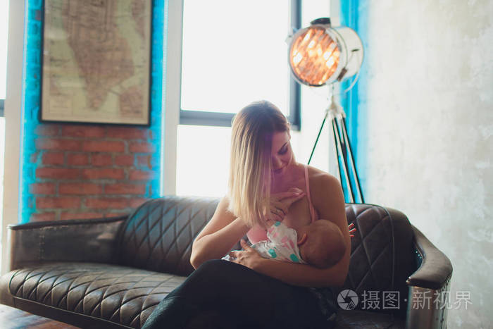 母乳喂养的妇女母乳喂养婴儿在现代阁楼内部.极简主义的丑闻设计.