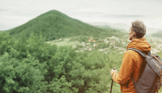 探险家背包族年轻人带着徒步旅行杆看着户外的山。