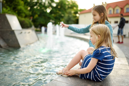 两个可爱的小女孩在阳光明媚的夏日在城市喷泉旁玩耍