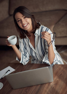 微笑的现代女孩使用笔记本电脑和喝咖啡的肖像。