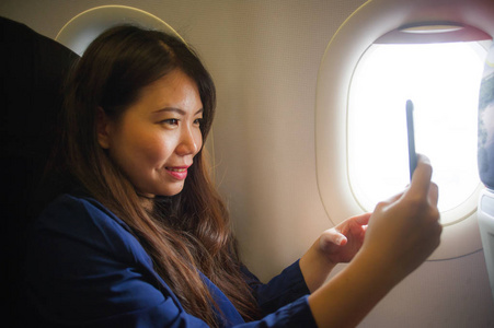 年轻快乐美丽的亚洲女性在机舱内出差，微笑愉快用手机自拍自画空中旅行旅游等概念