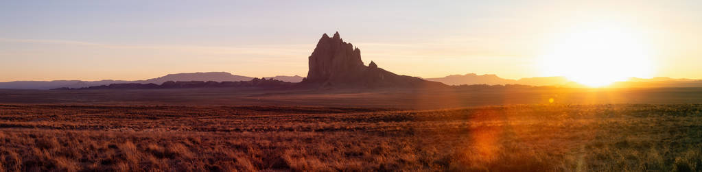 在一个充满活力的日落期间，一个干燥的沙漠的全景景观和一个山峰的背景。 在新墨西哥州的Shiprock，美国。