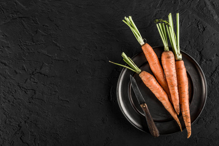 新鲜胡萝卜在深色石头背景上的盘子上。 食物概念图顶视图复制空间