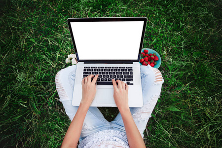 年轻的女人在夏天的草地上使用和打字笔记本电脑。 自由职业者在户外公园工作。