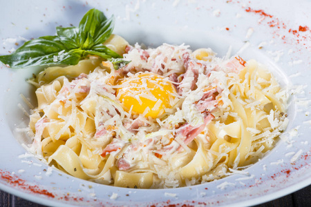 在深色木制背景意大利菜的盘子上放着肉火腿鸡蛋帕尔马干酪罗勒和奶油酱的费特uccine意大利面。 餐桌上的配料
