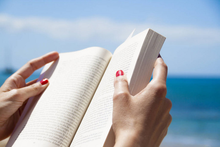 女人双手抱着和读一本书在海滩上
