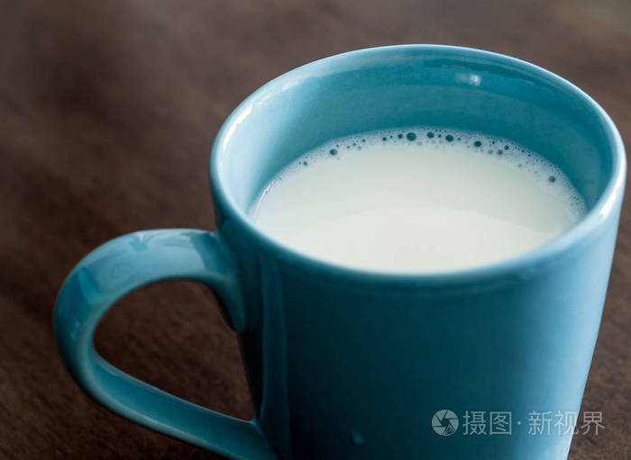 在木制和顶部玻璃桌上的蓝色杯子里的牛奶