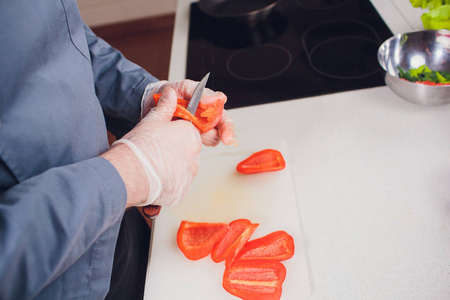 在切菜板上切甜红辣椒。男性用刀切辣椒。从上面看