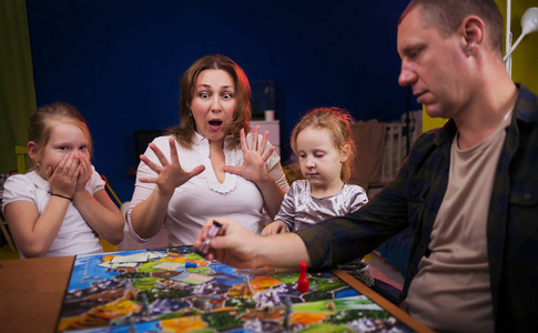 棋盘游戏概念。 一家人正在家里玩棋盘游戏。 棋盘游戏场许多数字硬币和沙漏。 四个人在脸上玩持卡片的快乐情绪。