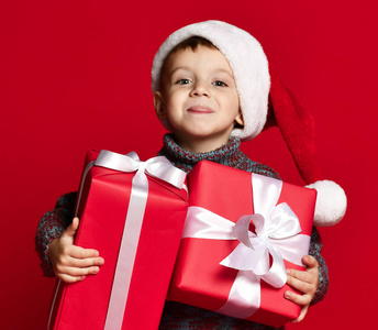 面带笑容搞笑儿童手持圣诞礼物的圣诞老人的红色帽子。圣诞节概念