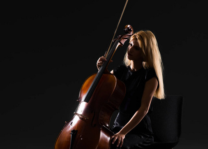 年轻女孩在孤立的黑色背景下玩大提琴