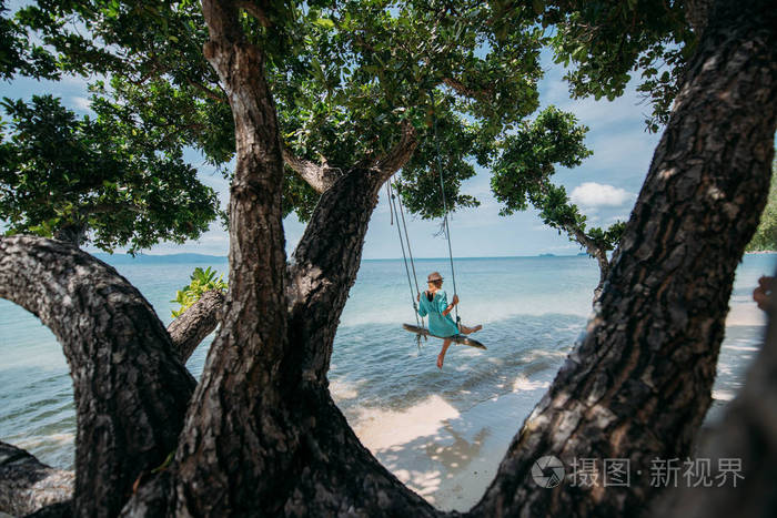 一个年轻的女人在海边一棵大树的树荫下荡秋千海滩上的女孩在热带岛屿