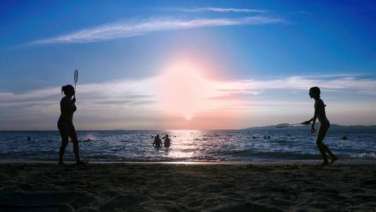 轮廓。日落时人们在海滩上打羽毛球