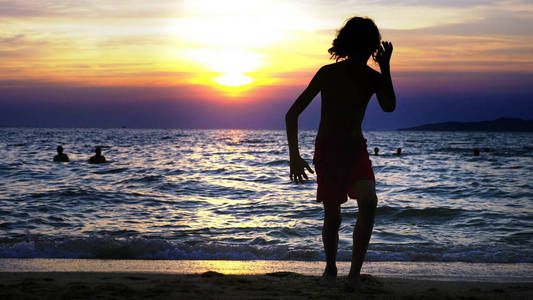 剪影一个男孩在海日落的背景, 滑稽的少年男孩在日落的背景下跳舞在海的背景下
