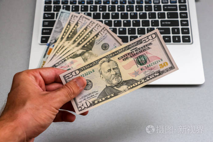 手拿一个50美元钞票笔记本电脑键盘在后台.