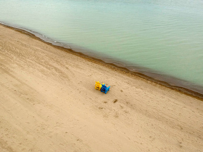 两把沙滩椅在海滩上,沙滩上,傍晚的灯光在绿水附近. 空中俯视.照片