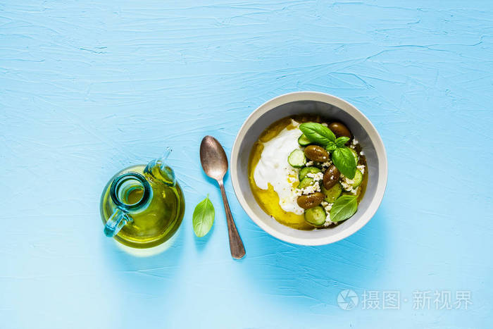 希腊酸奶与橄榄法塔奶酪黄瓜橄榄油和罗勒在蓝色背景上的平躺