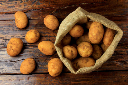 从种植园收获的新鲜和生土豆，放在木制桌子上的乡村袋子里。 顶部视图