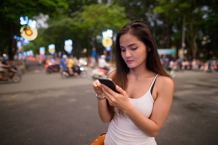 年轻美丽的亚洲旅游妇女使用手机户外