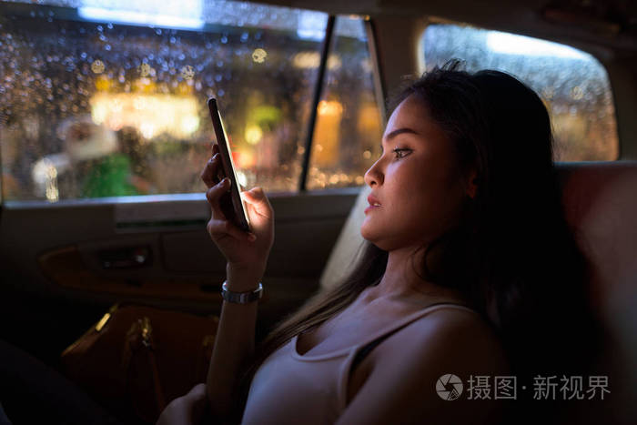 晚上坐在出租车上的年轻美女晚上用手机