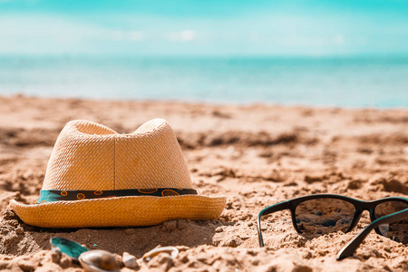 太阳镜和帽子在沙滩上对抗绿松石海。 热带海滩上的旅游和度假概念。 海滩上阳光明媚的快乐一天。