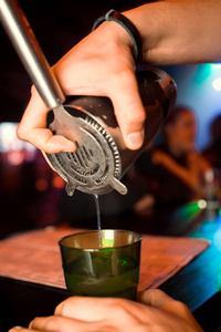 男酒保正在酒吧背景下从摇床到玻璃上倒酒. 酒吧服务员在工作.照片