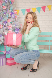 漂亮的女孩穿着蓝色的毛衣和牛仔裤，在她白色的房间里玩得很开心，房间里装饰着巨大的糖果糖果和带蝴蝶结的可爱的圣诞树