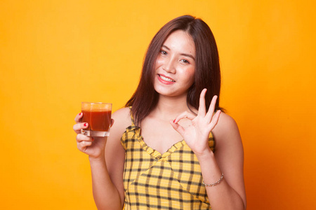 年轻的亚洲女人在黄色背景下表现出对番茄汁的满意