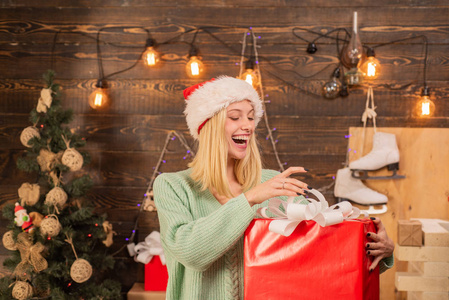 木制背景上的圣诞装饰品和礼品盒。真正的情感。在圣诞树前与圣诞节礼物箱子的年轻妇女