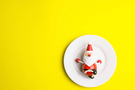 圣诞节时，白色盘子上的小圣诞老人被隔离在黄色背景上