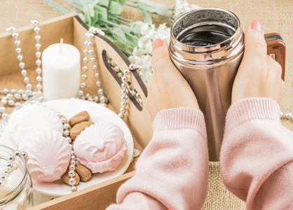 s hands on a hot cup of tea. Nearby is a wooden tray with candle