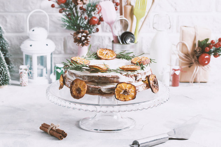用迷迭香和干柑橘片装饰的玻璃架上的圣诞蛋糕。 寒假作文肉桂礼品盒金属勺子厨房用品工具。