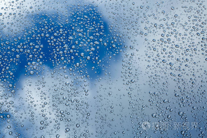 有多云背景的窗户玻璃表面有雨滴。