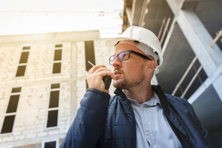 男总工程师戴白色安全安全帽，在检查施工现场时使用对讲机。 发展和建筑业概念