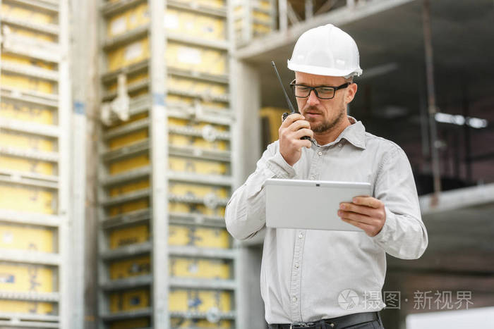 男总工程师戴白色安全安全帽与对讲机和平板检查施工现场.