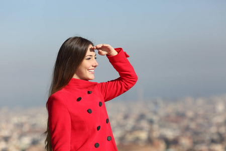 冬天穿红色童子军的快乐女人，手在额头上，有城市背景