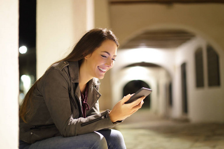 幸福的女人晚上坐在街上用智能手机