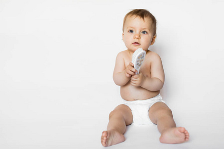 一个被烟熏的女婴的肖像，头发刷隔在白色的背景上。 穿着白色尿布的漂亮女婴正在玩毛刷。 婴儿护理及保健概念