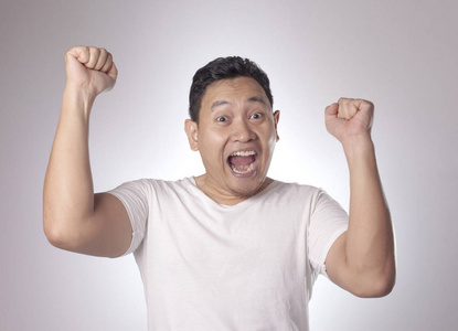 有趣的亚洲年轻人的肖像展示了胜利的姿态,惊讶地张开嘴.举起双手照片