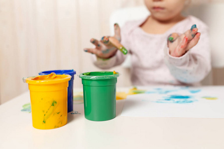 美丽的小女孩画与手指油漆在一张白纸上。幼儿园或在家中的空闲时间的创造性儿童发展