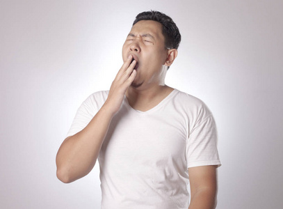 打哈欠亚洲困乏滑稽的亚洲年轻人打哈欠,坐着睡觉,灰色背景的半身像