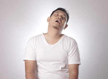 坐着睡觉困乏滑稽的亚洲年轻人打哈欠,坐着睡觉,灰色背景的半身像照片