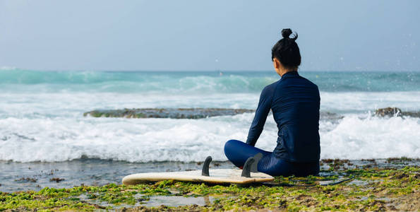 坐在礁石上看海浪的冲浪女子图片