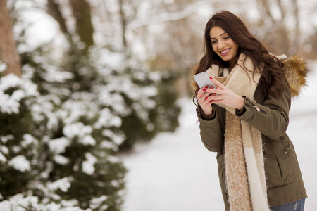 冬天户外带着手机微笑的年轻女子的画像