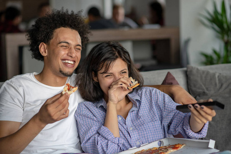 幸福的夫妇一边吃比萨饼一边看电视。浅景深，对人关注