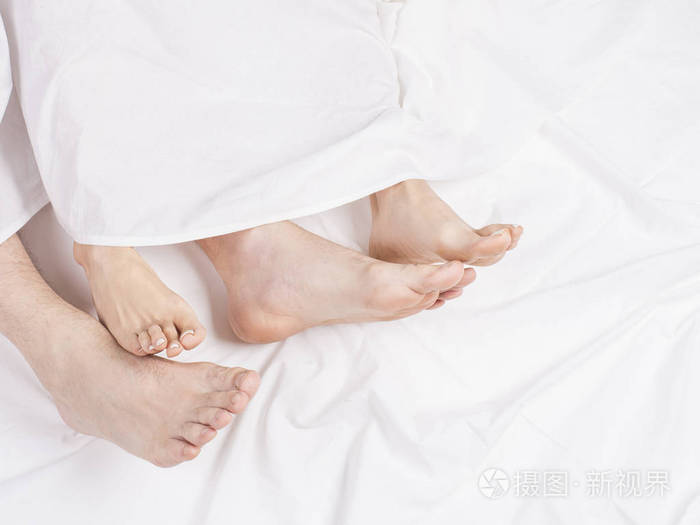 双脚并排睡在舒适的床上. 在白色毯子下的床上闭上脚.