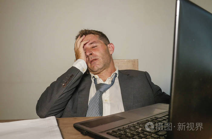 年轻沮丧压力大的商务男士西装革履地在办公室工作手提电脑桌上忙得不